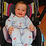 baby, child, car_seat, smiling, onesie, floral_pattern, indoor, happy, infant, seat_belt, head_support, padded_seat, person, cute, young_child, clothing, face, comfort, floor, wooden_floor