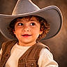 toddler, child, cowboy_hat, curly_hair, brown_vest, cream_sweater, smile, portrait, warm_lighting, closeup, cute, fashion, indoor, soft_light, face, eyes, clothing, person, happy, background_blur