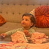 Victoria Grace is registered to the contest to win money with this photo: toddler, child, party_hat, pink_clothing, glass_table, sofa, cushion, window_blinds, indoor, curly_hair, baby_clothes, cute, curious_expression, seated, home_interior, tabletop, orange_cushion, soft_lighting, birthday, casual
