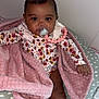 Brooklyn is registered to the contest to win money with this photo: baby, infant, pacifier, pink_bow, blanket, floral_clothing, socks, cushion, heart_pattern, cute, child, indoor, soft_texture, portrait, smiling, young, person, comfortable, baby_girl, seated
