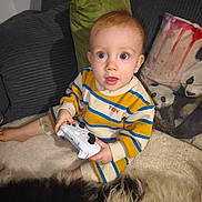 Edouard participe au concours pour gagner de l'argent avec cette photo : toddler, child, controller, gaming, striped_clothing, pillow, panda, blanket, sofa, indoors, curious, wide_eyes, cozy, couch, furniture, plush, young_child, sitting, home, portrait