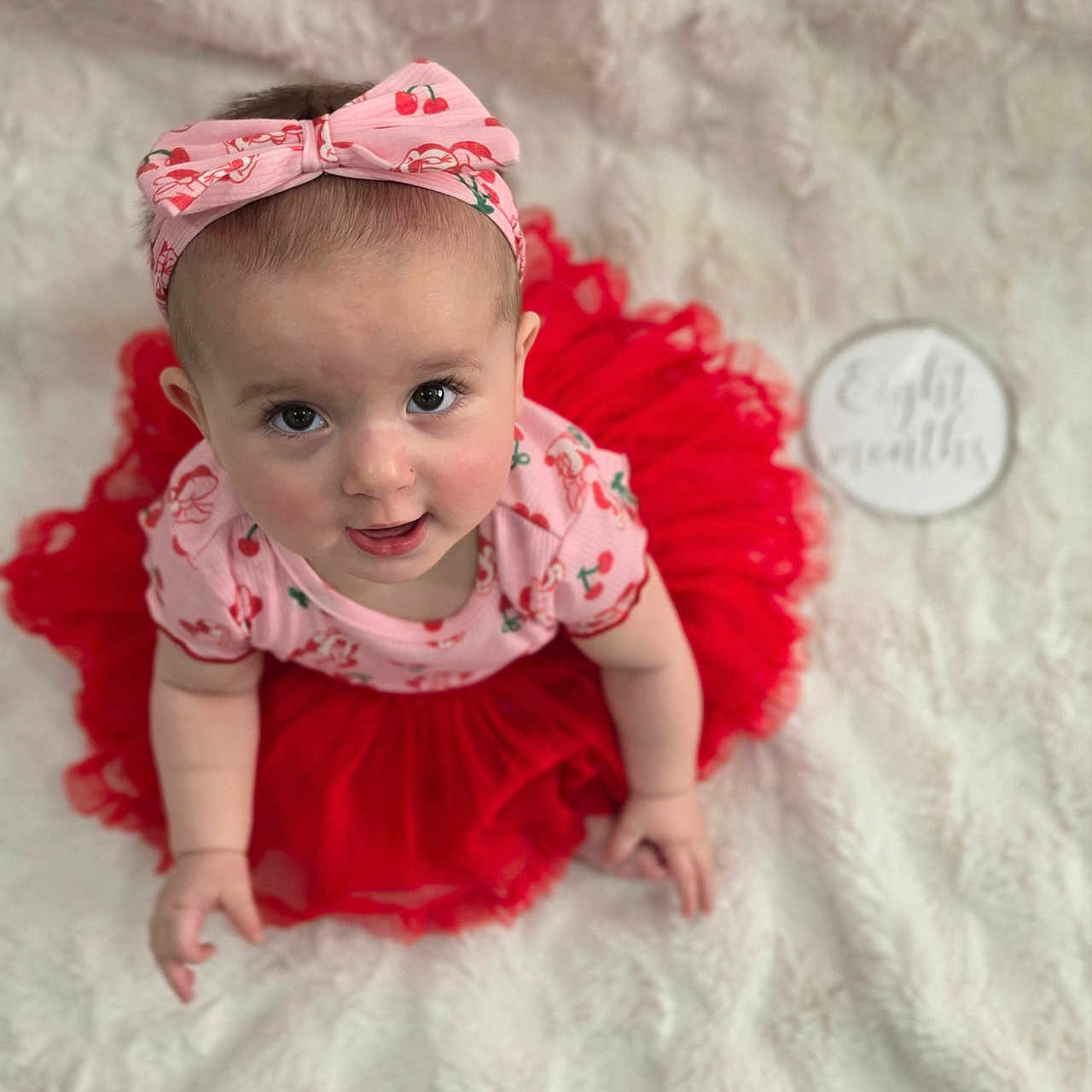 Amaya is registered to the contest to win money with this photo: baby, child, tutu, headband, pink, red, cherry_pattern, cute, portrait, soft_blanket, white, infant, smiling, looking_up, sitting, clothing, adorable, indoor, person, baby_fashion