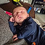 baby, sleeping, blanket, blue_clothing, pacifier_clip, indoor, living_room, television, furniture, hand, face, peaceful, cozy, child, person, soft, resting, home, comfort, casual