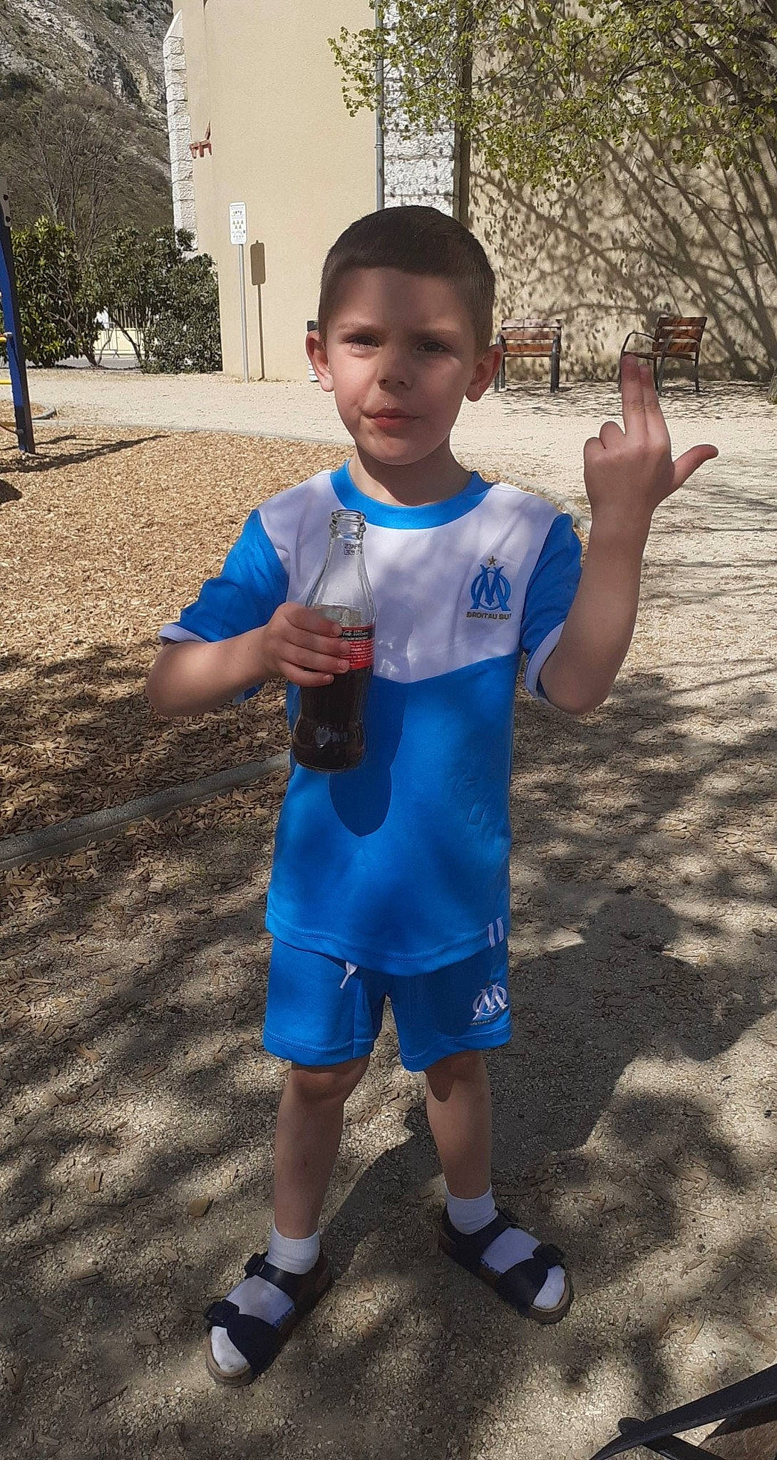 Angelino a rejoint le concours — aidez-le/la à gagner de superbes lots ! azure, blue, child, drinkware, electric_blue, finger, fun, gesture, happy, leisure, person, plastic_bottle, recreation, shorts, sleeve, t_shirt, thumb, toddler, tree, vacation