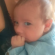 Kélyo a rejoint le concours — aidez-le/la à gagner de superbes lots ! adult, baby, blue_jacket, child, closeup, clothing, comfort, ear, face, hair, hand, head, indoor, infant, necklace, person, portrait, skin, sucking_fingers, warm_light