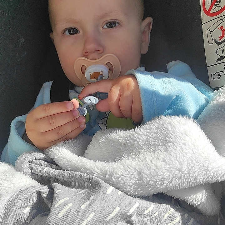 Emilio participe au concours pour gagner de l'argent avec cette photo : baby, pacifier, blanket, child, infant, blue_clothing, car_seat, cozy, soft_texture, holding, face, portrait, young_child, indoor, cute, small_hands, expression, seated, comfort, focused