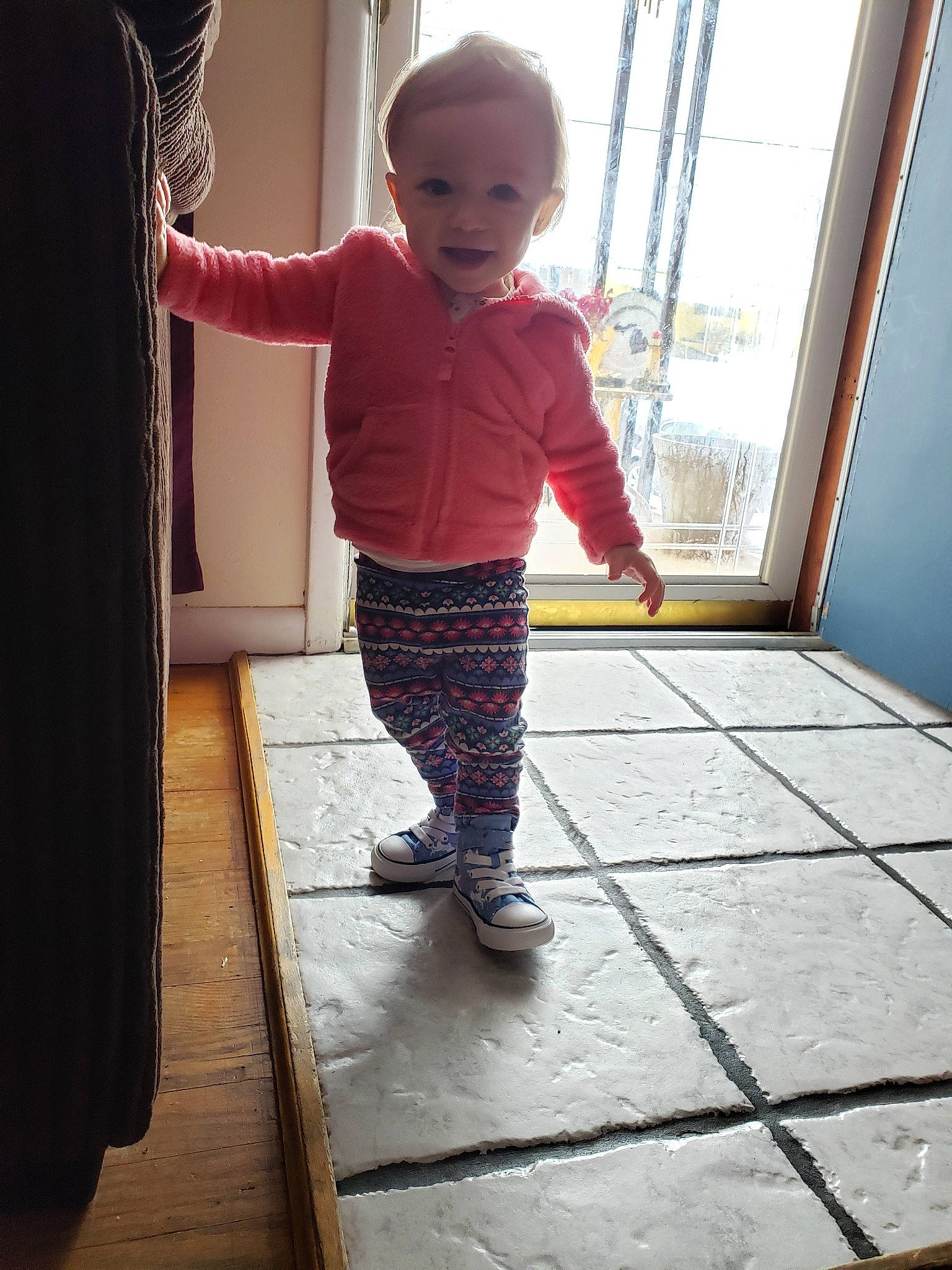 Anastasia is registered to the contest to win money with this photo: baby, child, curious, door, floor, flooring, leg, pattern, person, shoe, standing, toddler, window