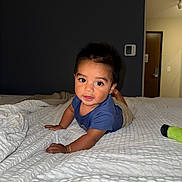 Norlan is registered to the contest to win money with this photo: baby, child, infant, portrait, indoors, bedroom, bed, blanket, blue_shirt, sitting, crawling, smiling, curious, dark_hair, face, eyes, hands, thermostat, door, toy