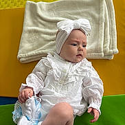Annie is registered to the contest to win money with this photo: baby, child, white_clothing, headband, bow, blanket, colorful_background, mat, sitting, infant, cute, indoors, soft_texture, sock, footwear, portrait, young_child, expression, hand, person