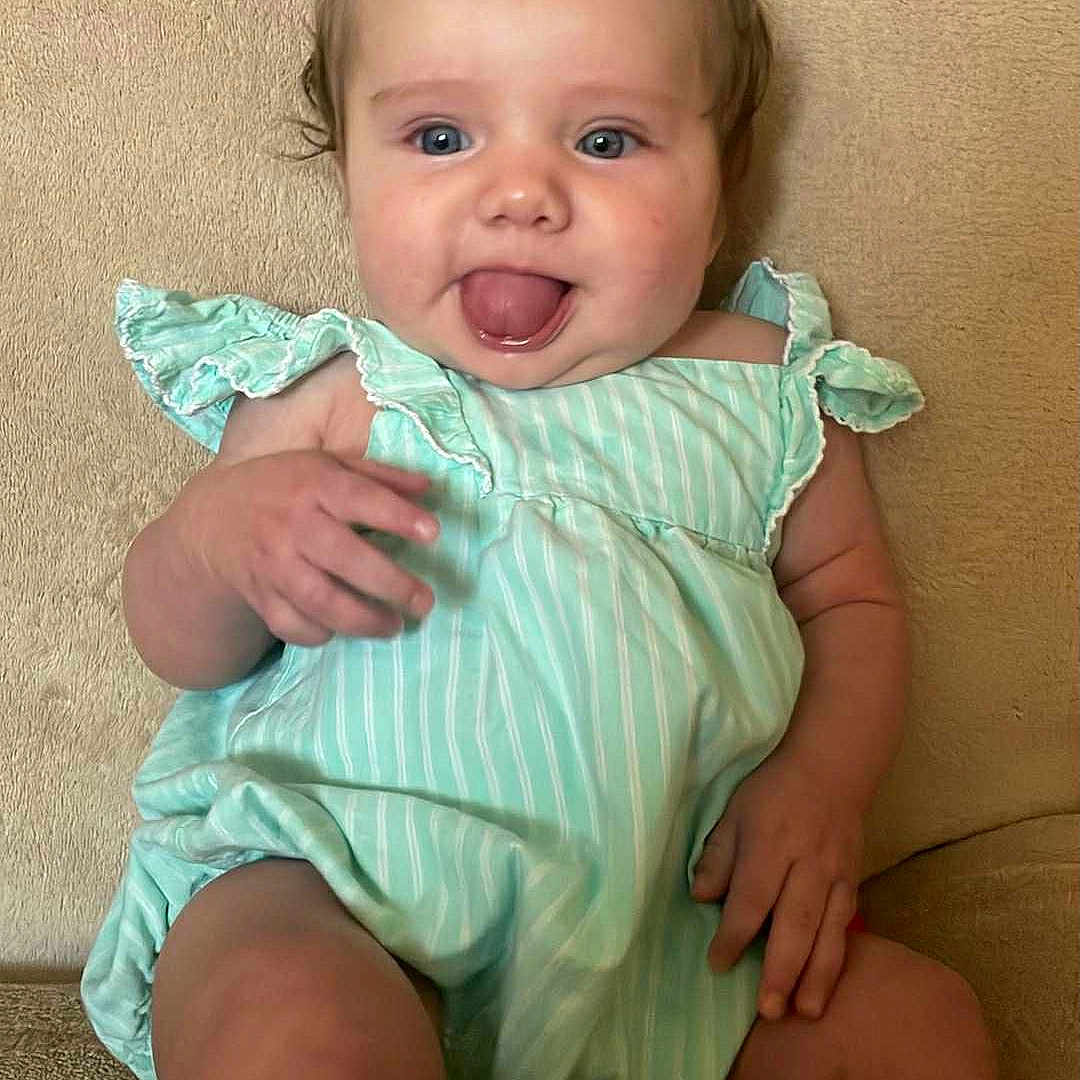 Kacelynn is registered to the contest to win money with this photo: baby, blue_eyes, child, clothing, couch, cute, green_dress, hair_bow, hand, happy, head, indoor, infant, legs, person, portrait, sitting, skin, smiling, tongue_out