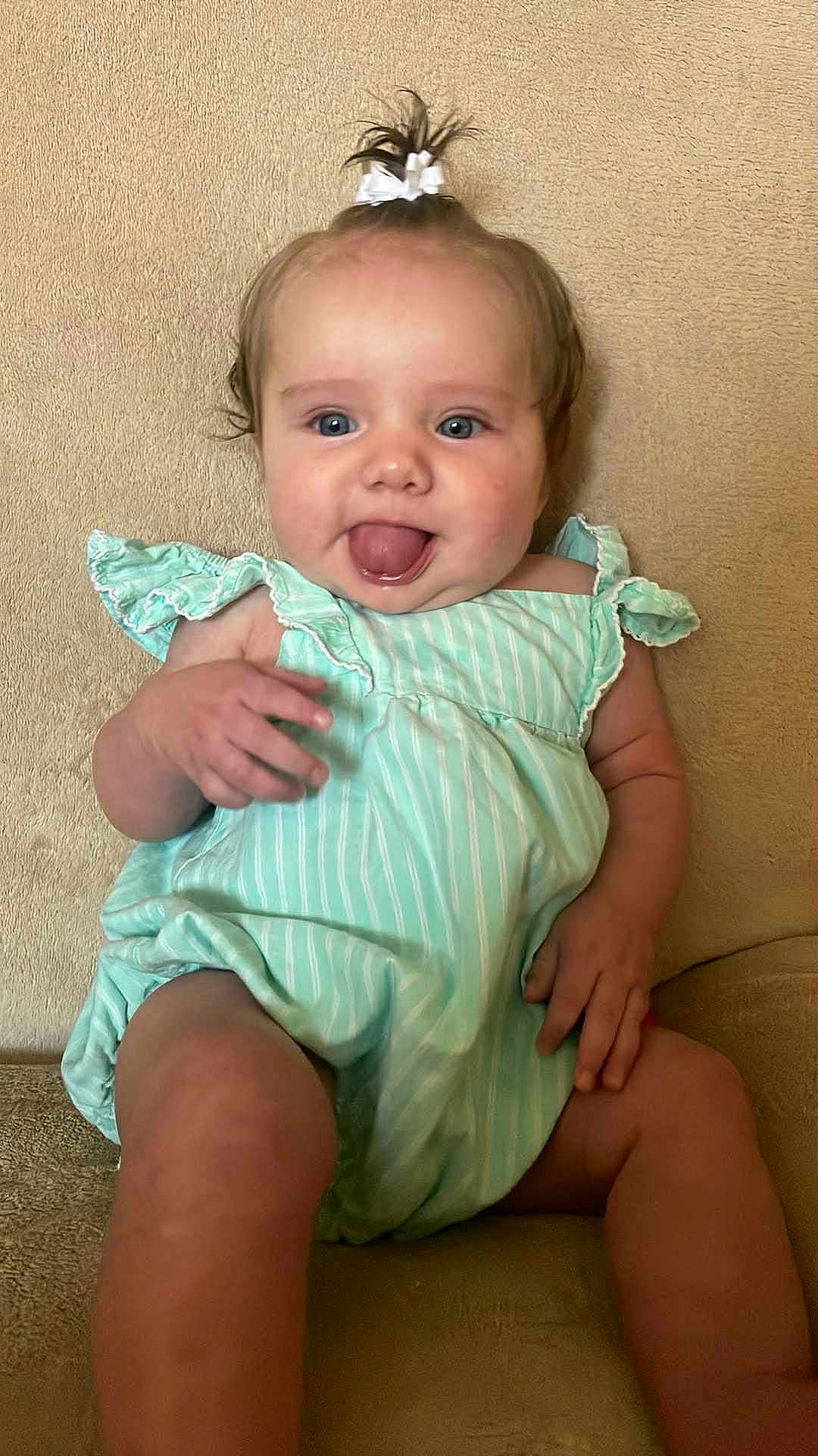 Kacelynn is registered to the contest to win money with this photo: baby, blue_eyes, child, clothing, couch, cute, green_dress, hair_bow, hand, happy, head, indoor, infant, legs, person, portrait, sitting, skin, smiling, tongue_out