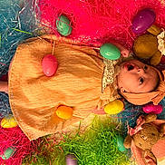 Lainey joined the competition — help win amazing prizes! baby, child, easter_eggs, plush_toys, headband, dress, colorful, easter_grass, pink, blue, green, yellow, orange, purple, toy_bunny, surprised_expression, celebration, holiday, indoors, laying_down