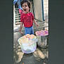 child, water_balloons, bucket, outdoor, play, happy, concrete, clothing, person, summer, fun, colorful, shorts, red_shirt, smile, daylight, stairs, building, barefoot, water