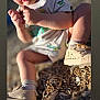 toddler, child, outdoor, sunlight, wood_chips, shoes, curious, hands, short_sleeve_shirt, socks, natural_light, focus, skin, legs, ground, texture, young_child, exploration, casual_clothing, daylight