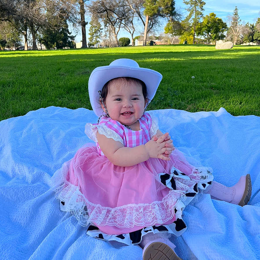 Emery joined the competition — help win amazing prizes! baby, bonnet, clothing, dress, face, footwear, grass, hat, head, nature, outdoors, park, person, photography, plant, portrait, shoe, sitting, sunhat, tree