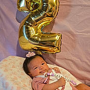 Cataleyah is registered to the contest to win money with this photo: baby, balloon, celebration, child, cozy, cushion, cute, fabric, flower, headband, indoors, infant, lying_down, newborn, number_two, pink, portrait, smile, soft_texture, warm_lighting