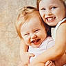 children, siblings, toddler, preschooler, smiling, laughing, happy, hugging, cuddling, portrait, indoors, close_up, blonde_hair, young_faces, family, sitting, pink_shirt, blue_clothing, warm_lighting, black_border