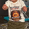 Dylan is registered to the contest to win money with this photo: toddler, child, baby, smiling, happy, standing, portrait, indoor, shirt, graphic_tshirt, pants, socks, curly_hair, dark_skin, face, teeth, furniture, rug, home, photography