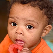 Dylan joined the competition — help win amazing prizes! baby, child, infant, portrait, close_up, curly_hair, brown_skin, orange_clothing, teething_ring, hand, fingers, eyes, face, mouth, curious, indoors, photography, looking_at_camera, colorful, safe