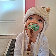 Sacha a rejoint le concours — aidez-le/la à gagner de superbes lots ! toddler, child, pacifier, hat, bear_ears, plush_toy, indoor, floor, white_clothing, blue_eyes, cute, baby, smile, sitting, tile_floor, door, wall, striped_rug, looking_up, cozy