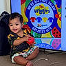 ball, carpet, child, clothing, colorful, floor, furniture, hair, happy, indoor, patterned_clothing, person, play, reflection, screen, sitting, smiling, television, toddler, toy