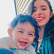 Wahaj is registered to the contest to win money with this photo: child, toddler, woman, smile, happy, indoor, portrait, curly_hair, long_hair, floral_clothing, casual, family, love, joy, person, face, window, light, candid, together