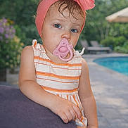 Cindy is registered to the contest to win money with this photo: toddler, child, pacifier, headband, pink, striped_dress, outdoor, poolside, cushion, summer, portrait, blue_eyes, hair, hand, skin, daylight, relaxing, garden, blurred_background, cute