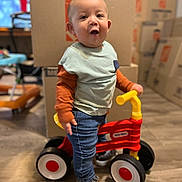 Kairi joined the competition — help win amazing prizes! cardboard_boxes, casual_clothing, child, curious, expression, face, flooring, furniture, happy, home, indoor, jeans, long_sleeve_shirt, moving, person, playtime, sneakers, standing, toddler, toy_bike