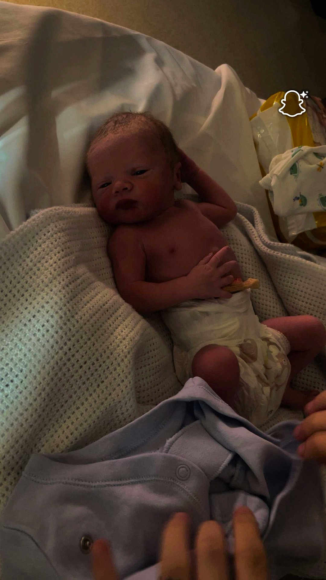 John-Peter joined the competition — help win amazing prizes! baby, newborn, infant, diaper, blanket, bed, bassinet, hand, parent_hand, skin, face, eyes_open, swaddle, clothing, snapchat_logo, soft_lighting, portrait, cozy, nursery, resting