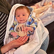 Gabriel joined the competition — help win amazing prizes! baby, infant, newborn, one_month, milestone_sticker, blanket, couch, adult_hand, baby_hand, hoodie, plaid_jacket, striped_shirt, jeans, portrait, indoor, cozy, bokeh_background, eyes, cheeks, skin