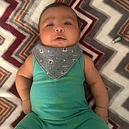 Rayan is registered to the contest to win money with this photo: baby, infant, child, romper, bib, patterned_blanket, zigzag, green_clothing, grey_bib, football_pattern, lying_down, cute, chubby_cheeks, indoors, portrait, face, arms, legs, curious, expression