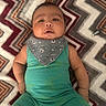 baby, infant, child, romper, bib, patterned_blanket, zigzag, green_clothing, grey_bib, football_pattern, lying_down, cute, chubby_cheeks, indoors, portrait, face, arms, legs, curious, expression