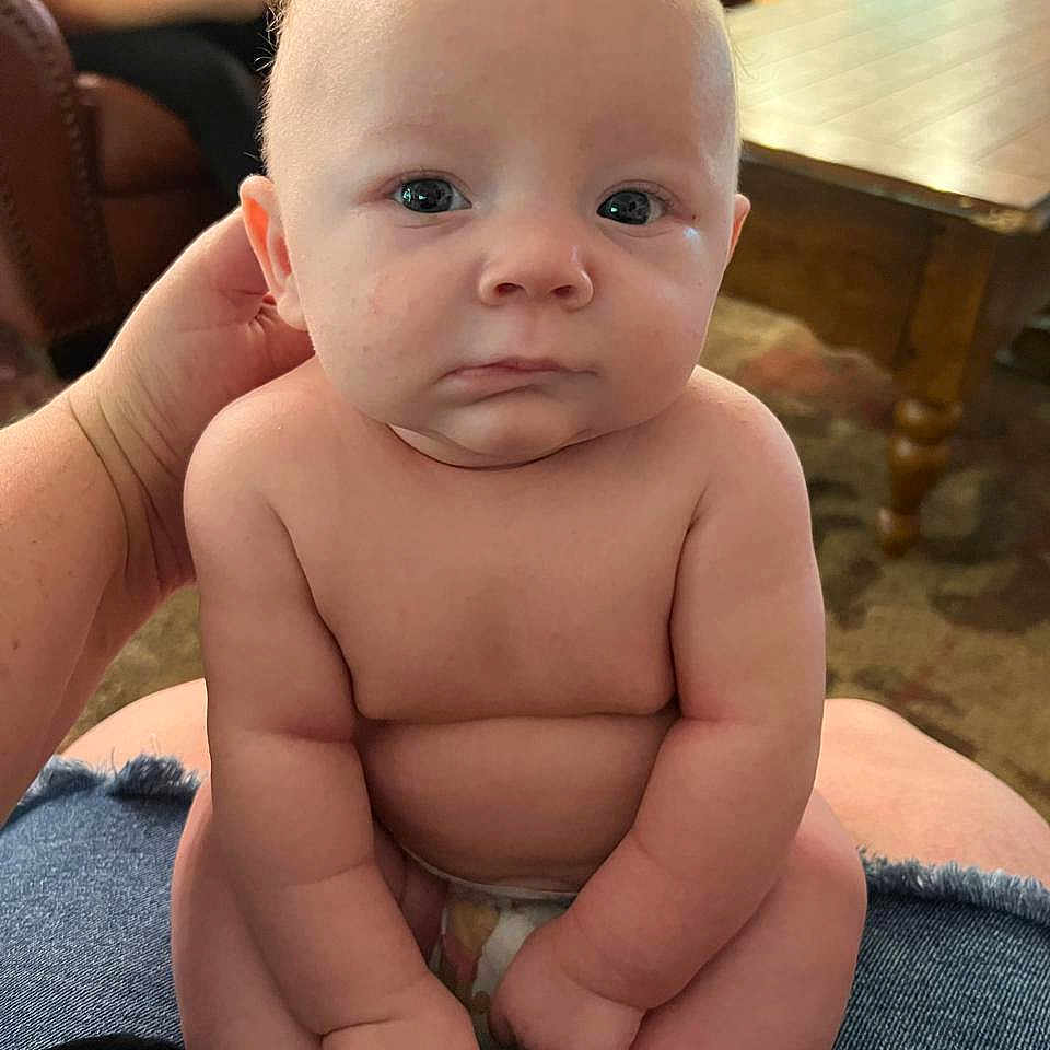 Dominic joined the competition — help win amazing prizes! arms, baby, carpet, child, couch, diaper, expression, face, furniture, hand, indoor, infant, legs, living_room, naked_torso, person, sitting, skin, support, wooden_table