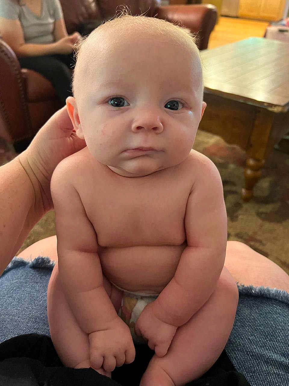 Dominic joined the competition — help win amazing prizes! baby, infant, child, sitting, naked_torso, diaper, hand, person, indoor, living_room, furniture, couch, wooden_table, carpet, skin, face, arms, legs, expression, support