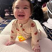 Ember is registered to the contest to win money with this photo: baby, child, crawling, smiling, happy, pajamas, floral_pattern, indoor, mattress, toy, yellow_toy, face, person, cute, infant, hands, head, carpet, home, expression