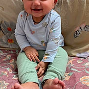 Takshvi joined the competition — help win amazing prizes! baby, child, smiling, sitting, indoor, cute, happy, clothing, long_sleeve_shirt, pants, barefoot, toes, quilt, floral_pattern, pillow, hair, face, hands, eyes, infant