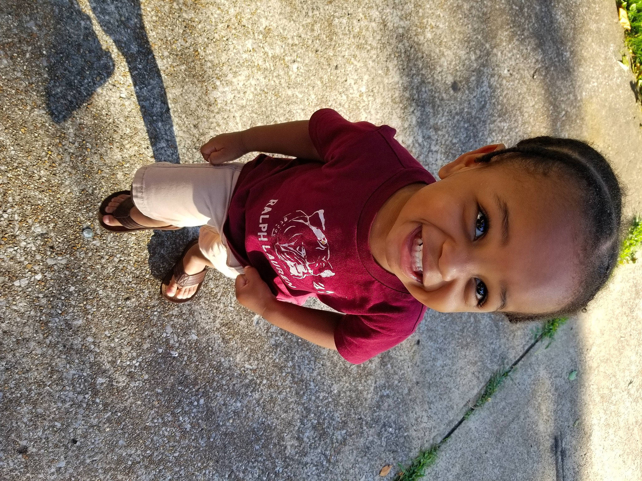 Diego is registered to the contest to win money with this photo: asphalt, child, facial_expression, fun, grass, happy, hat, human_leg, joy, leg, leisure, mammal, person, plant, public_space, recreation, sitting, skin, smile, toddler