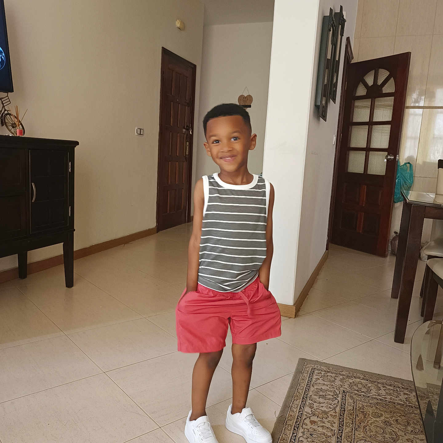 Ayden participe au concours pour gagner de l'argent avec cette photo : boy, cabinet, casual_clothing, chair, child, door, happy, home_interior, indoor, living_room, person, rug, shorts, smiling, standing, table, tank_top, tile_floor, wall_decor, white_sneakers