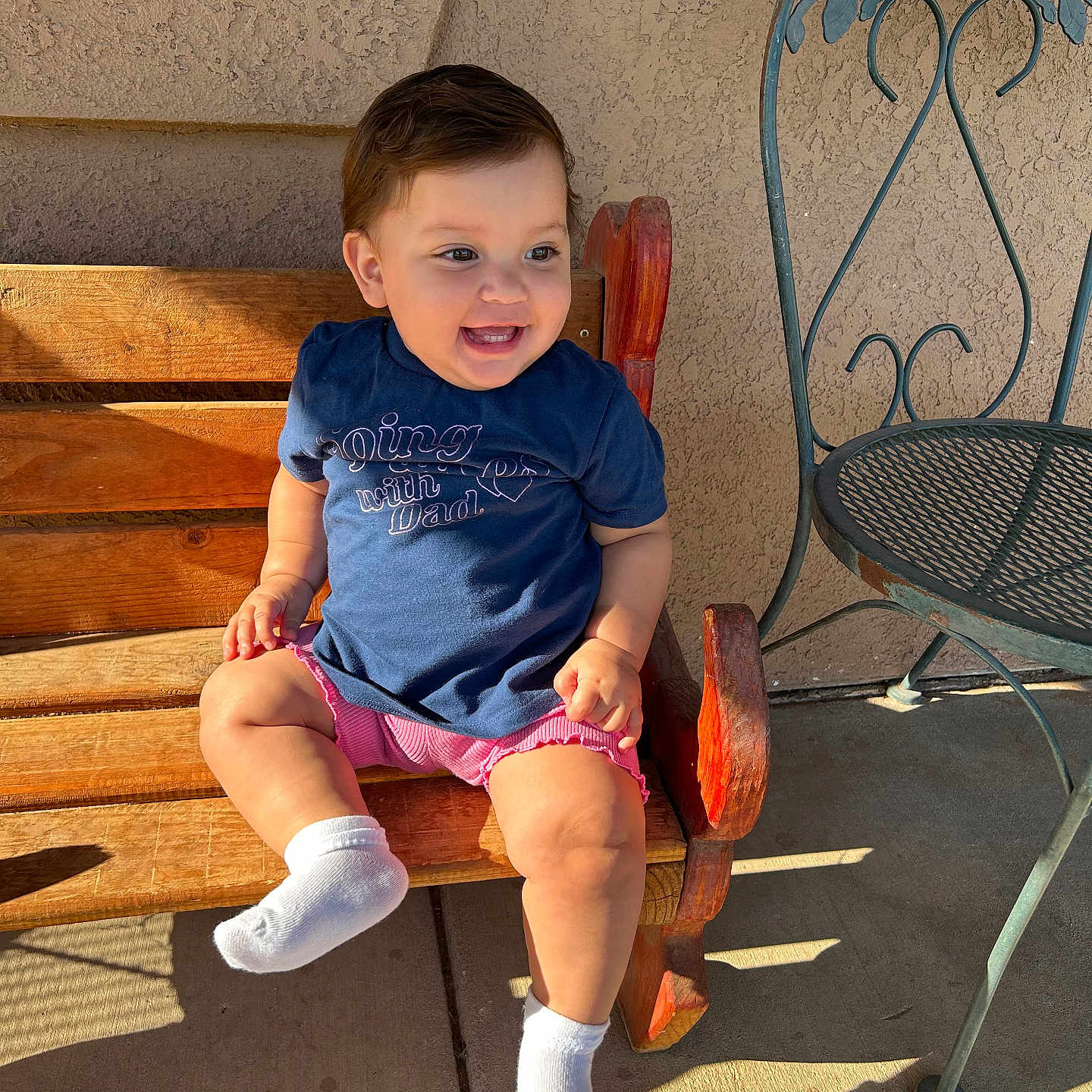 Leia Sophia joined the competition — help win amazing prizes! bench, child, clothing, cute, daylight, happy, metal_chair, outdoor, person, seat, shadow, shirt, shorts, smiling, socks, sunlight, texture, toddler, wall, wood