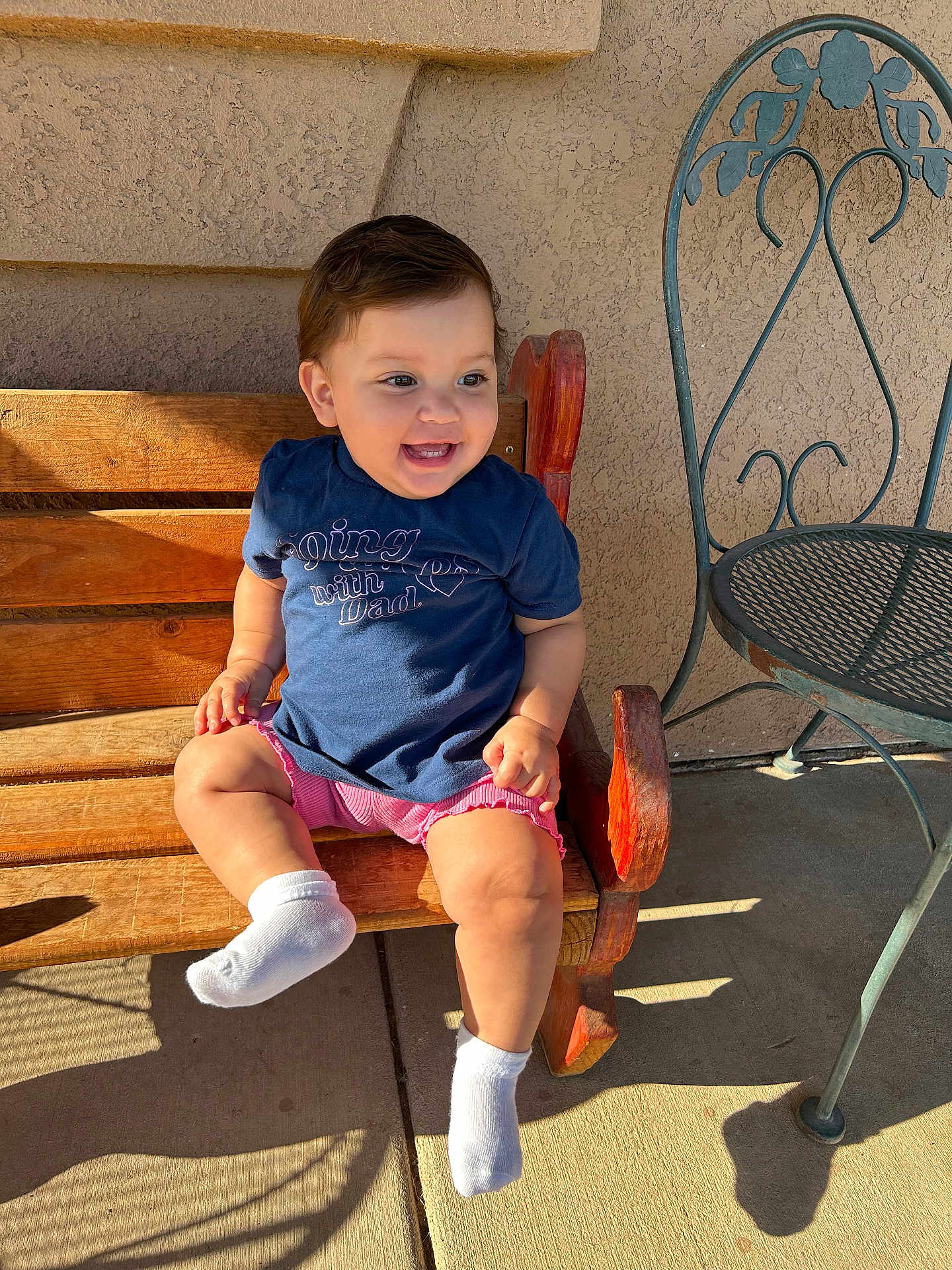 Leia Sophia joined the competition — help win amazing prizes! toddler, child, smiling, bench, wood, outdoor, sunlight, shadow, wall, clothing, shorts, shirt, socks, happy, person, seat, metal_chair, texture, daylight, cute
