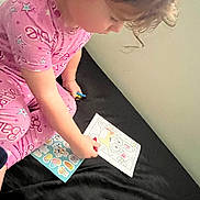 Elianna joined the competition — help win amazing prizes! child, pajamas, pink_clothing, coloring, cartoon, paper, stickers, curly_hair, bed, black_bedspread, indoor, activity, person, young_child, art, drawing, concentration, cute, play, fun