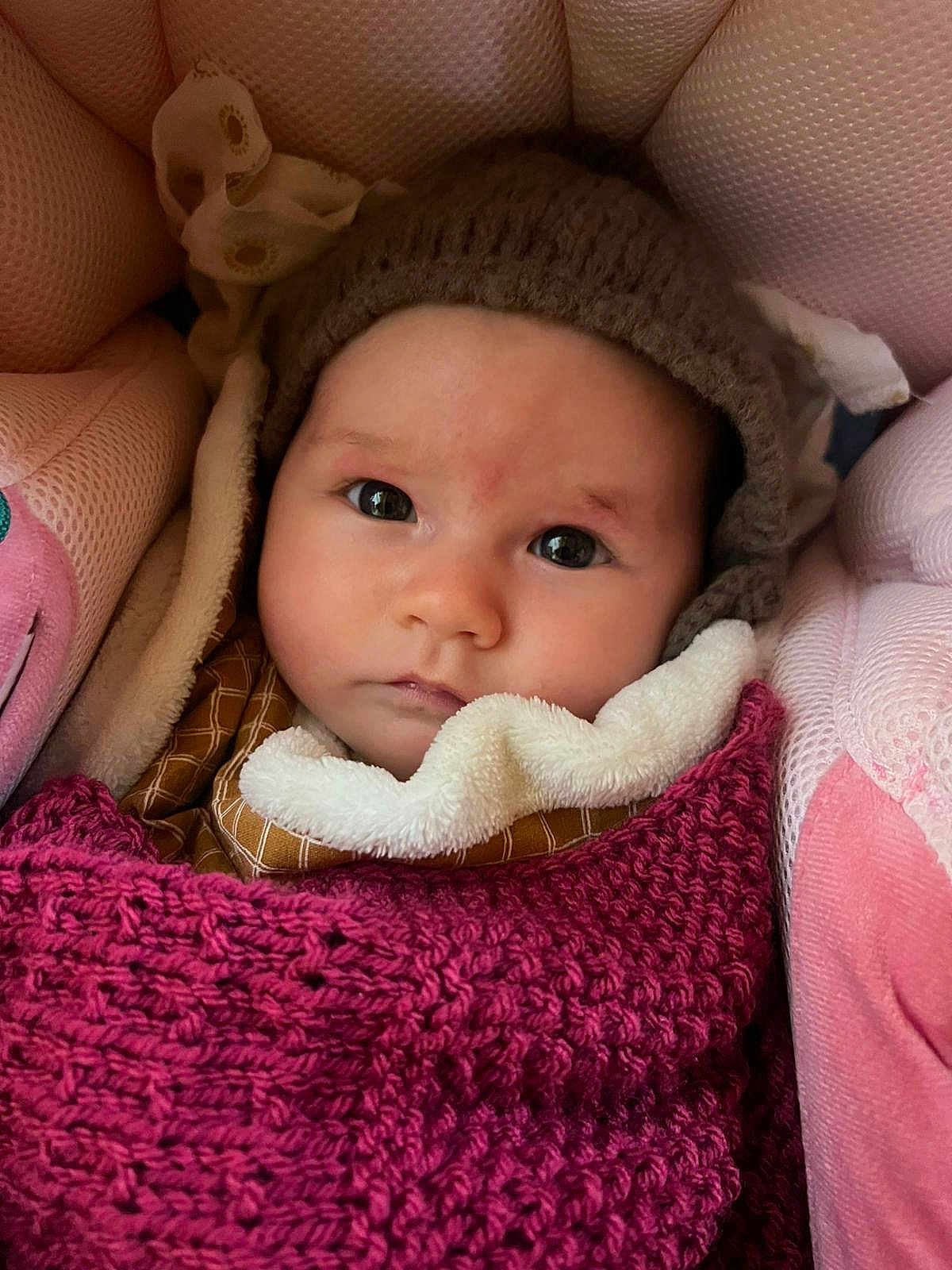 June participe au concours pour gagner de l'argent avec cette photo : baby, infant, face, knit_hat, blanket, pink, cushion, warm_clothing, wrapped_up, indoors, closeup, portrait, child, soft_texture, cozy, cute, looking_at_camera, young, headwear, seated