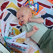 Callahan joined the competition — help win amazing prizes! baby, infant, child, portrait, lying_down, smiling, tongue_out, eyes_open, striped_shirt, green_clothing, baby_book, toy, owl_toy, rattle, playpen, blanket, patterned_bedding, colorful, indoor, cute