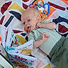 baby, infant, child, portrait, lying_down, smiling, tongue_out, eyes_open, striped_shirt, green_clothing, baby_book, toy, owl_toy, rattle, playpen, blanket, patterned_bedding, colorful, indoor, cute