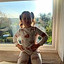 Laila is registered to the contest to win money with this photo: child, girl, window, pajamas, standing, hands_on_hips, playful, funny_face, pigtails, indoor, natural_light, sunlight, smile, home, casual_clothing, curtains, background_blur, confident, young, cozy