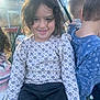 child, smiling, outdoor, swing, curly_hair, white_shirt, patterned_clothing, black_pants, playground, greenhouse, sunlight, friends, children, happy, casual_clothing, daytime, grass, play, fun, group