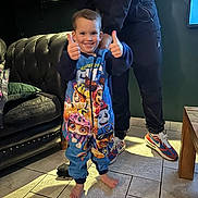 Feroze is registered to the contest to win money with this photo: child, toddler, pajamas, paw_patrol, thumbs_up, barefoot, smiling, indoor, living_room, couch, floor, tile, person, adult, sneakers, table, happy, home, clothing, furniture