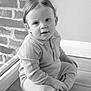 toddler, child, sitting, indoor, window, brick_wall, floor, cozy_clothing, portrait, black_and_white, curious, young_child, casual, texture, soft_light, hands, face, hair, home, relaxed