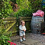 Harbi joined the competition — help win amazing prizes! toddler, child, outdoor, garden, greenery, wooden_gate, barrel, scooter, toy, path, stones, plants, shoes, clothing, person, daylight, nature, happy, cute, smile