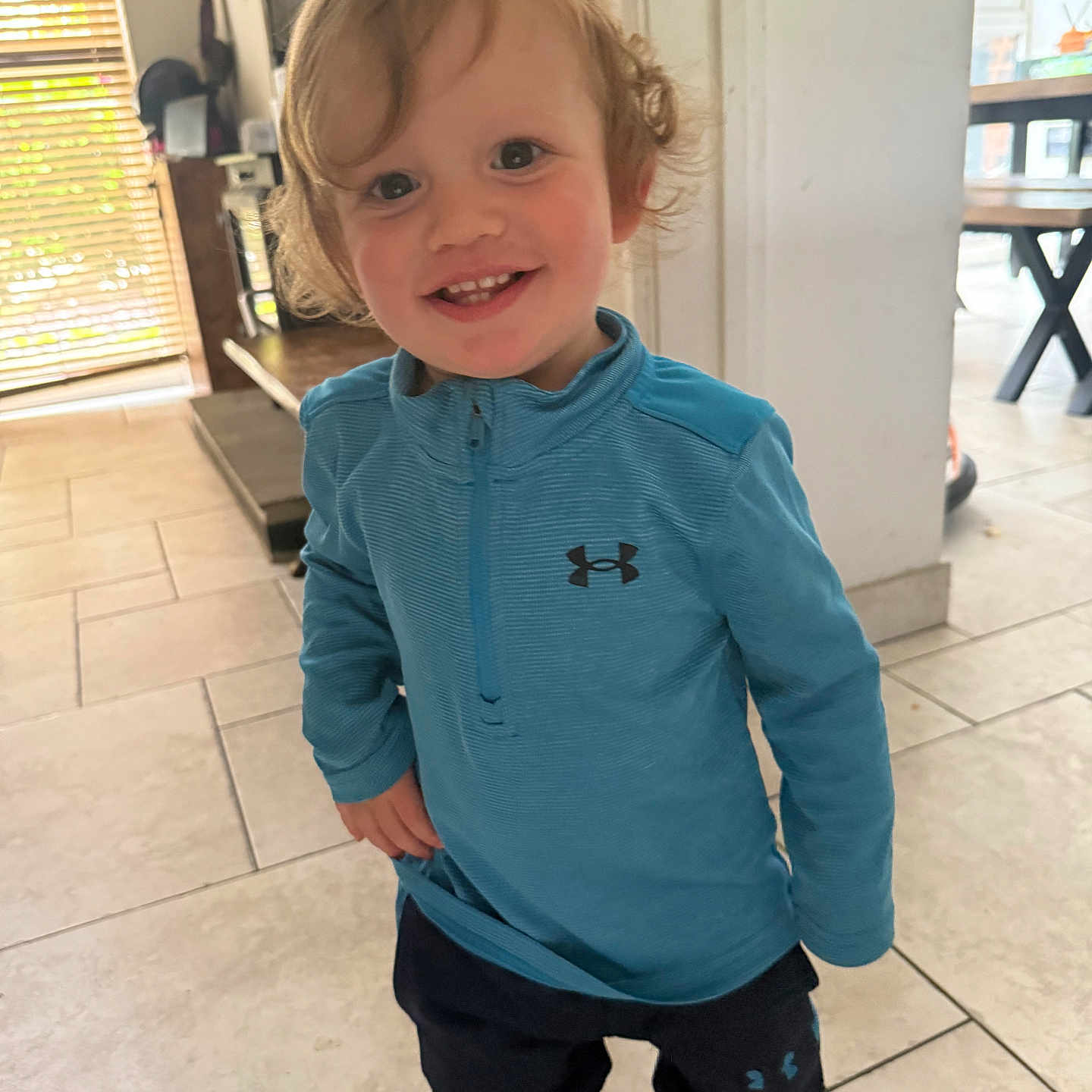 Harbi joined the competition — help win amazing prizes! blue_shirt, casual_clothing, child, curly_hair, cute, floor_tiles, furniture, happy, home, indoor, light, pants, person, playful, smiling, sneakers, standing, toddler, under_armour, window_blinds